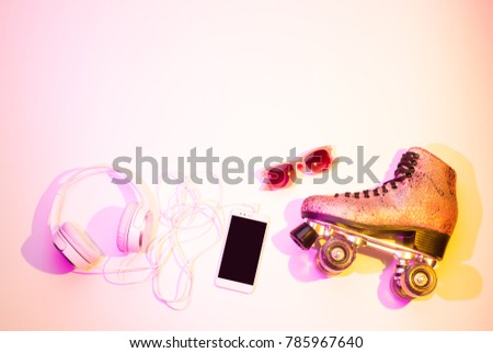 Retro pink glittery roller skates, mobile phone (smartphone), headphones and sunglasses captured from above (top view, flat lay). Fun, recreation and active lifestyle - background (free text space).