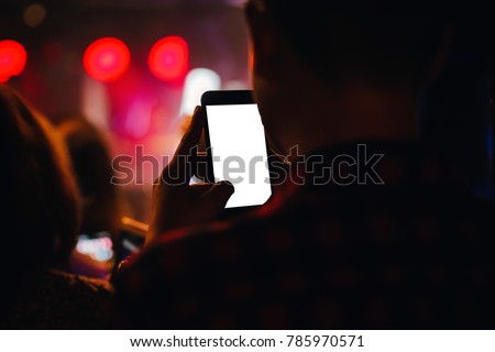 Hand holding smart phone with blank white screen. Photo shot blurry party and concert of event Background and copy space. Smart phone white screen. Technology and lifestyle