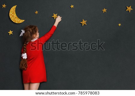 Little curly girl in red dress reach out for the stars and the moon in the sky. Dreaming concept with a wish Good night.