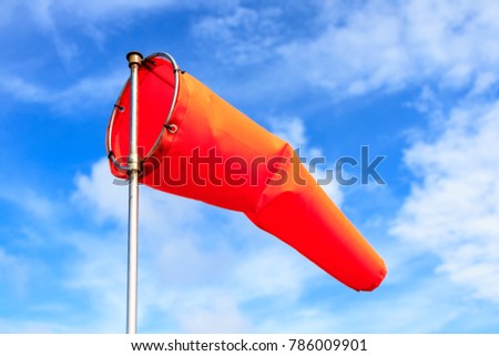 Orange wind sock in blue sky and white cloud background.