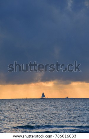 A boat sailing through the cloudy weather at sunrise, far in the ocean