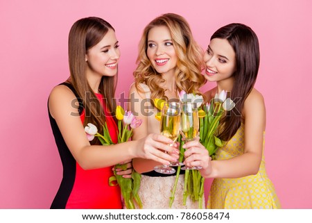Three, charming, pretty, trendy girls celebrating women's day, 8 march, holding colorful tulips and drinking, clinking glasses with champagne over pink background