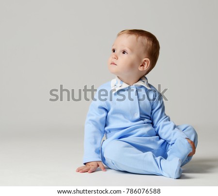Infant child baby boy kid toddler sitting in light blue body cloth looking at the corner on gray background