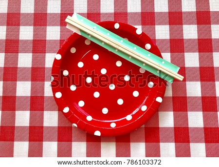 Closeup A red polka dot paper plate with wooden chopsticks set on red & white checkered pattern background. The concept of party accessories,picnic utensil,Food display.Top view. Selective focus.