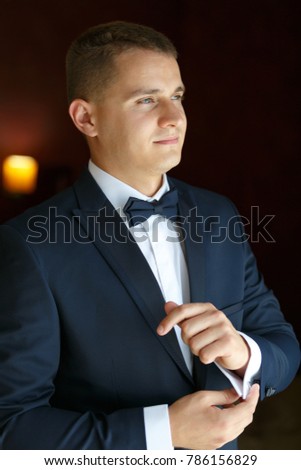 A confident elegant handsome young man buttons cufflinks and looks out the window. Vertically framed shot.