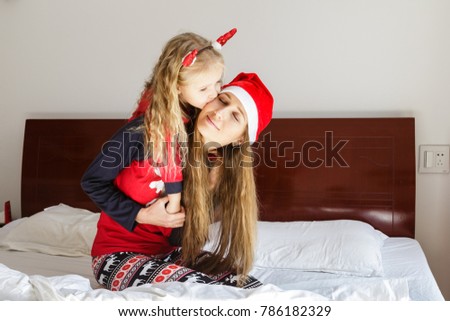 beautiful mother and daughter in their Christmas pajamas sit at home in the bedroom on the bed. daughter kisses mother on the cheek