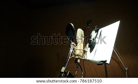 Microphone with shockmount and pop filter on tripod and note stand in recording sound studio video production.