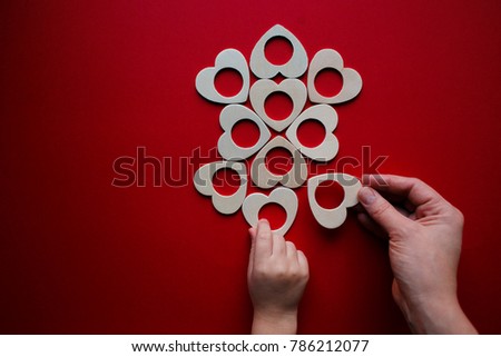 wooden details on red background. Assembled form in the form of an ornament. Heart shape of the details.Hands woman and child folding puzzle in red.