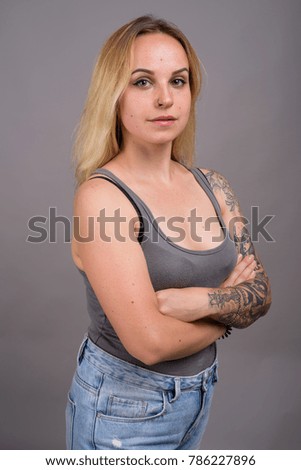 Studio shot of young beautiful blond woman with hand tattoos in Russian meaning "Belief and Truth" against gray background