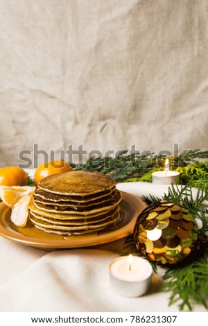 Pancakes with oranges on a Christmas table with candles