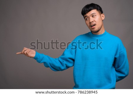 Studio shot of young Asian man wearing blue sweater against gray background
