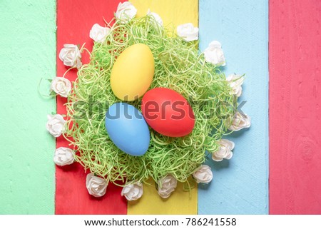 Easter arrangement with painted eggs on decorative grass, surrounded by small white roses, displayed on a background from multicolor wooden planks.