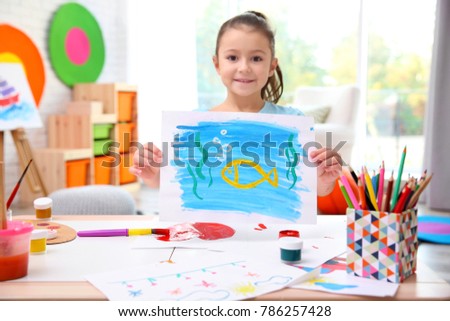 Little girl holding picture at table indoors