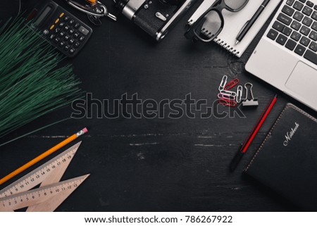 Office desktop. Laptop, camera, calculator, glasses, ruler, pen, pencil. On the black wooden surface. Top view. Free space for text.