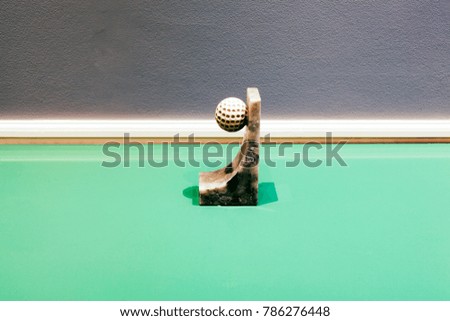 A golf ball with a marble base on top a glass green table as an abstract installation