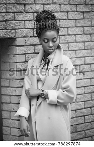 African girl with bright makeup and a blue coat is standing at the brick wall in the style of fashion black and white image