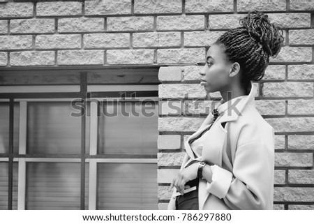 African girl with bright makeup and a blue coat stands in profile at a brick wall in the style of fashion black and white image