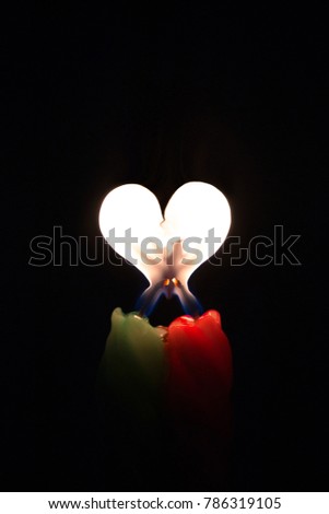 Two colored burning candles with a flame in the form of a heart on a black background