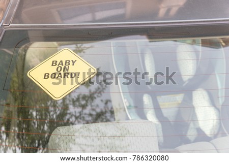 Baby On Board sticker on the car back windows. A blurred image of car seat is available in background.