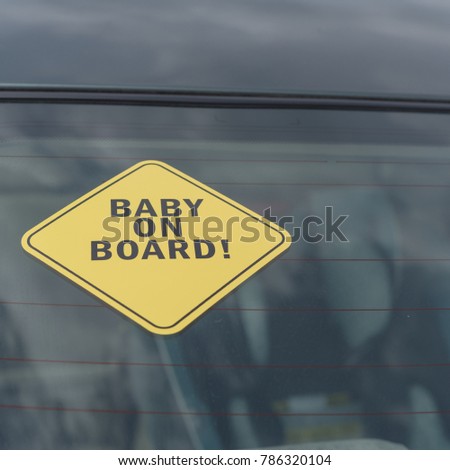 Close-up view of Baby On Board sticker on the car back windows. A blurred image of car seat is available in background.