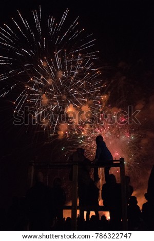 Silhouette indistinguishable family figures watching colourful firework display in dark at night