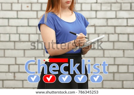 checklist. young woman hand holding a list with pen on brick wall background