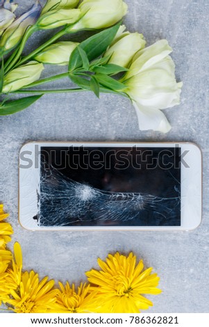 Flowers are spread around a mobile phone with a broken screen.