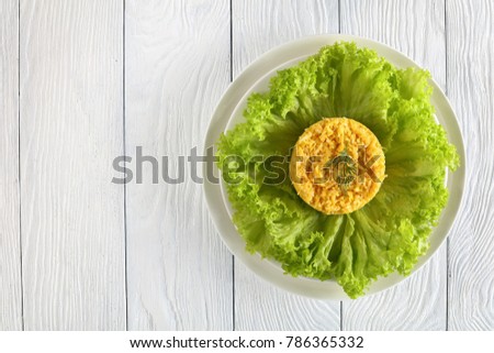 russian cheese salad with hard boiled eggs, mayonnaise and grated garlic on a white plate on wooden table, view from above