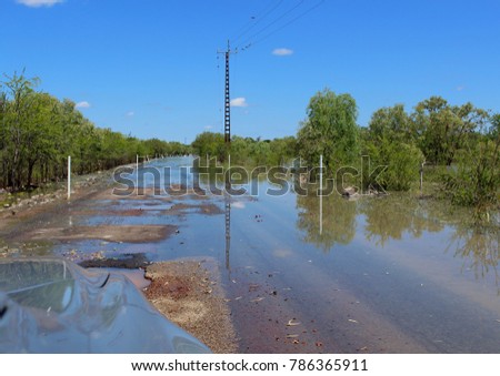 Landscape picture of a flooded road taken from a car framed against a bright blue sky, in Northern Territory, Australia