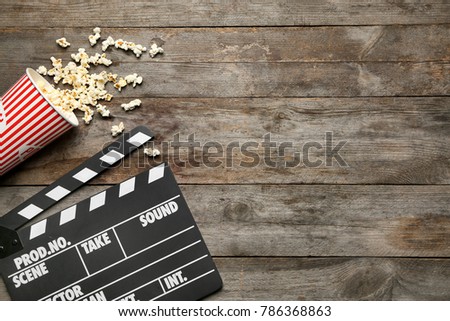 Movie clapper and popcorn on wooden background, top view