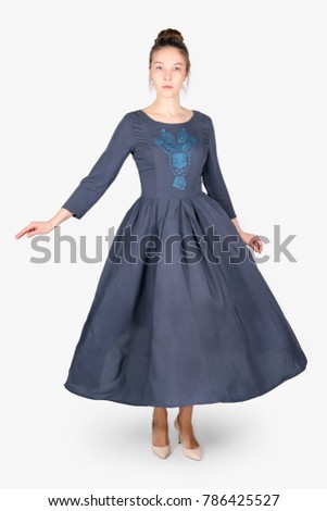 Female model wearing dress posing on grey neutral background. Beauty stylish woman proposing product, advertising gesture. Fashionable clothes in studio