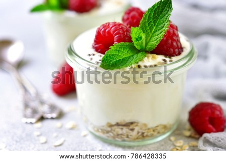 Two portions of homemade natural yogurt with oats,chia seed and fresh berries in a vintage glass jar on a light slate,stone or concrete background.Concept of healthy breakfast.