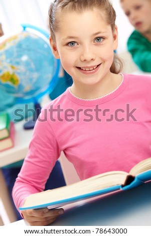 Portrait of smart schoolgirl with open book looking at camera
