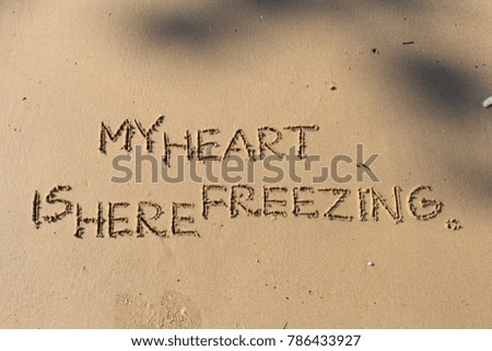 Handwriting  words "MY HEART IS HERE FREEZING." on sand of beach.