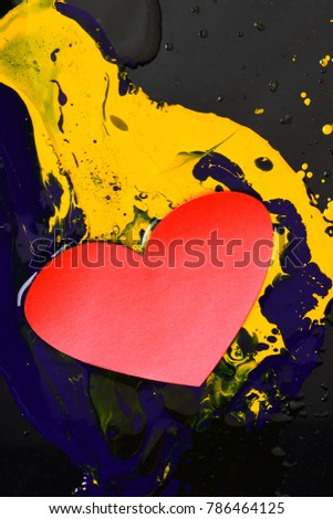 Heart made of paper lying on paints. Drops of blue and yellow oil or acrylic paint poured on black background. Paint splashes and love symbol. Valentines day and art concept.