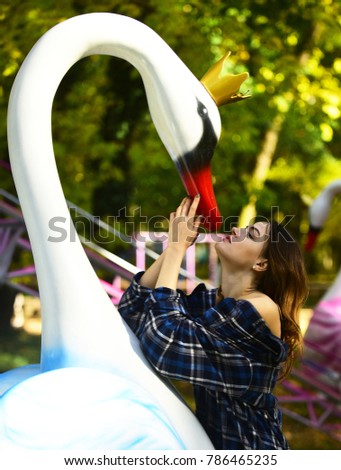 Woman and swan on green sunny park background. Girl with passionate face looks up. Lady and big steel sculpture representing tenderness and devotion. Femininity and love concept.