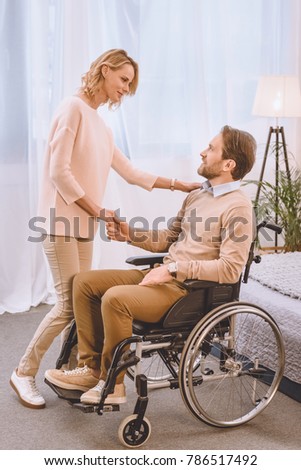 happy husband on wheelchair and wife holding hands in bedroom