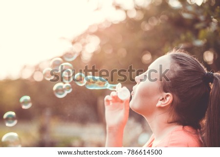 Pretty young brunette woman making soap bubbles during lovely summer sunset (warm filter, color toned image)