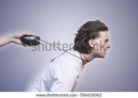 The human hand pulling young man with tied wire from computer mouse on the white background. Computer or game addiction concept. Selective focus and shallow DOF