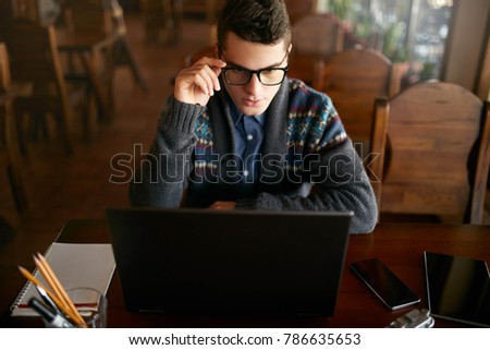 Businessman working with documents on laptop tablet and smart phone on table. Freelancer browsing web in cafe. Handsome hipster in knitted sweater holding glasses in his hand. Poor eyesight threatment