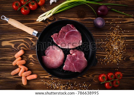 Raw pork steak in a frying pan with spices, cherry tomatoes, carrots, lettuce and onions