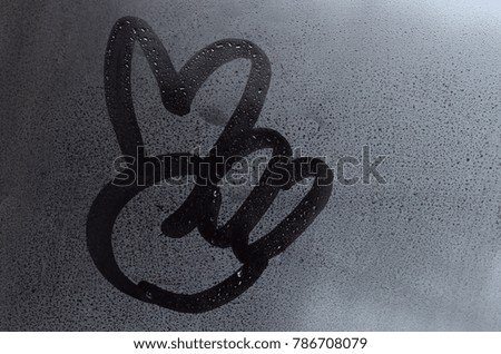 The image of the peace symbol is drawn with a finger on the surface of a misted glass window. Combination of two fingers