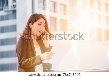 surprise businesswoman talking smartphone and holding paper ducument outdoors