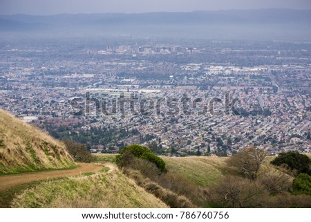 Aerial view of residential areas of San Jose, California on a rainy day; hiking trail in Sierra Vista park on the right; the city's financial district in the background; 