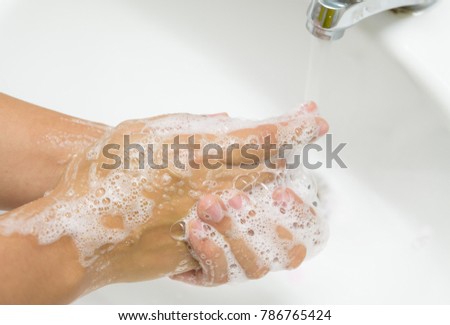 Woman washing hands with soap under the faucet with water  in the bathroom.