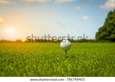 Golf ball on tee in green grass at golf course.