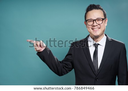 Portrait of asian businessman smile and points with finger to camera left on vintage blue background .