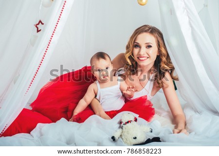 Happy cute little baby girl with mother. Christmas, dressed in red dres in decorated New Year room at home. Child good mood. Lifestyle, family and holiday  concept.