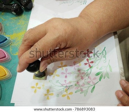Woman is working art, in the form   rubber stamp  and using a stamp colour ink.Rubber stamp by hand