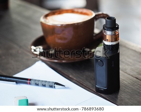 Close up shot of unidentified e-cigarette on coffee table with a cup of coffee in work environment refer to stress relief and nicotine addiction that help create work flow